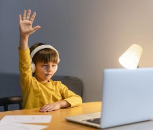 school-boy-yellow-shirt-taking-virtual-classes-raising-hand